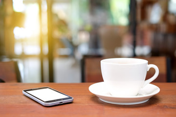 White coffee cup and smart phone on wooden table with blurred ca