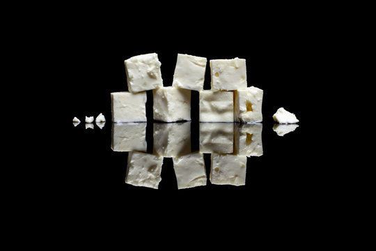 Seven blocks of feta cheese on black reflective background