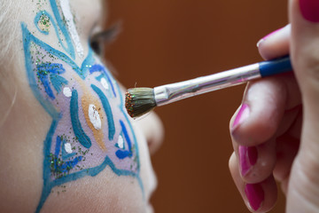 Visagist is painting butterfly on the face of a little girl