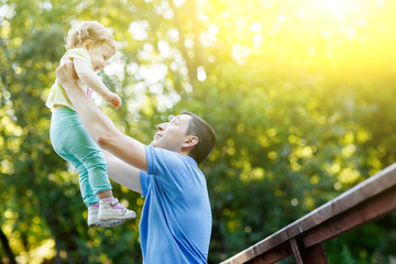 Young father holds little daughter in arms in park