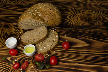 Bread slices decorated with cherry tomatoes with a cup of oil and salt lying on a wooden background