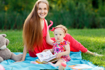 Young girl with her daughter sitting on plaid in park