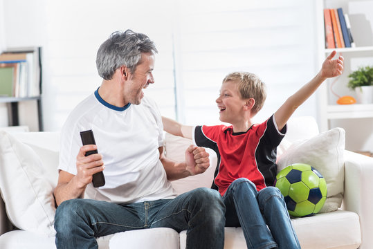 A father and his young son watching a football match on TV
