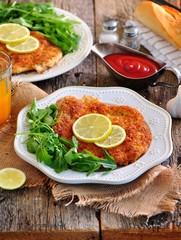 Pork schnitzel with organic arugula and lime on a old wooden background.