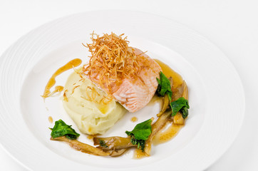 Salmon with mashed potatoes and gravy on a plate on a white background, closeup