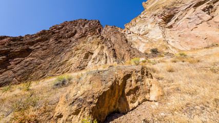 Unusual shaped rocks on the background of blue sky. The sheer rock walls. Beautiful landscape of yellow sharp cliffs. Dry yellow grass grows at the foot of cliffs. Smith Rock state park, Oregon