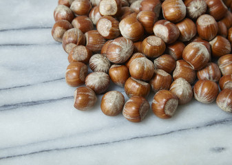 A pile of whole hazel nuts arranged on a white marble counter background