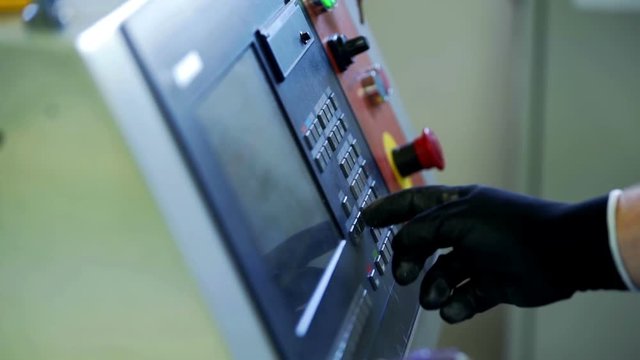 A worker is pressing a few buttons on the screen in the factory. He is wearing black protective gloves. Close-up shot.
