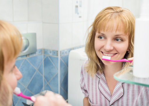 Portrait of happy woman cleaning her oral cavity caring about dental health. Pretty young female while brushing teeth in bathroom.