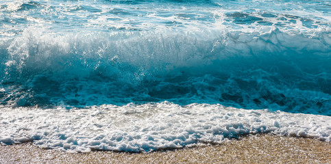 Waves breaking and spraying in Mediterranean summer sea. Sea view from beach. Blue water at sunny hot day.