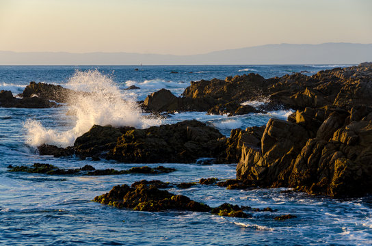 Wave crashing against rocks at sunset