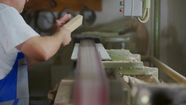A carpenter is shaping wood on a belt sander and then he is checking if it looks okay. Wide-angle shot.
