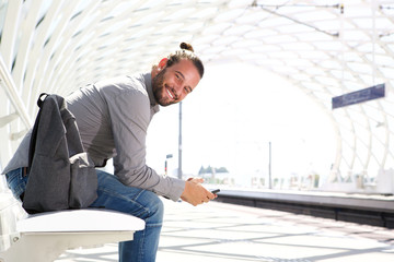 Smiling man with mobile phone and backpack at train platform