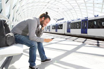 Smiling man sitting at train platform with cellphone