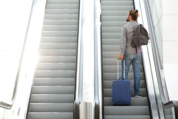 Traveling man going up escalator with suitcase and bag