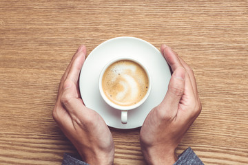 Male hands holding cups of coffee on rustic wooden table backgro