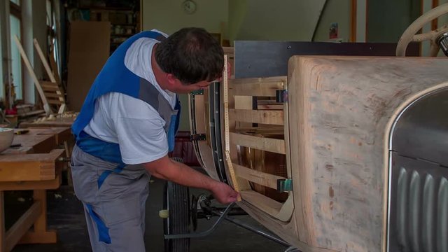 A middle-aged joiner is measuring the wooden door of a vintage car. He looks very dedicated. Close-up shot.
