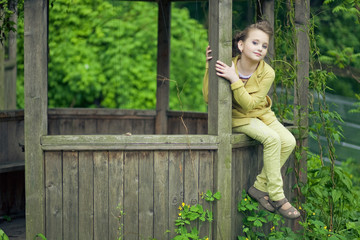 Obraz premium Little girl in yellow suit sits on the wooden pergola