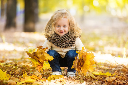 Joyful little girl in park in autumn with leaves in their hands