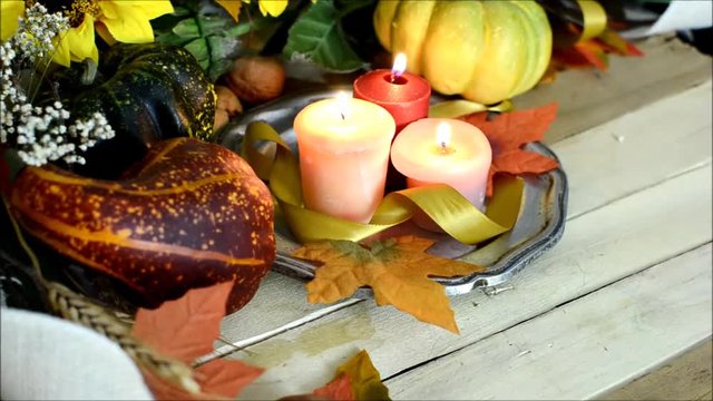 Thanksgiving scene with gourds and squashes, fall leaves and flickering candles on a rustic wooden table slowly rotating
