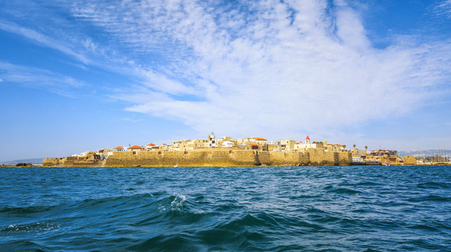 View from the sea to the ancient fortress city of Acre in Israel against the backdrop of a colorful sky.