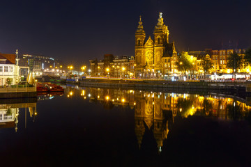 Fototapeta na wymiar Night city view of Amsterdam canal with Basilica of Saint Nicholas and its mirror reflection in the water, Holland, Netherlands. Long exposure.