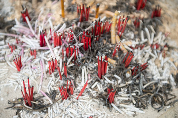 Clumps of red incense sticks and yellow candles stick up from the ashes at a Buddhist temple in Bangkok Thailand