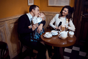 Happy father kisses his little blonde daughter while mom admires