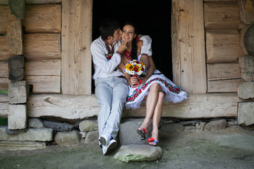 Groom in white suit kisses bride's cheek tender while they sit o