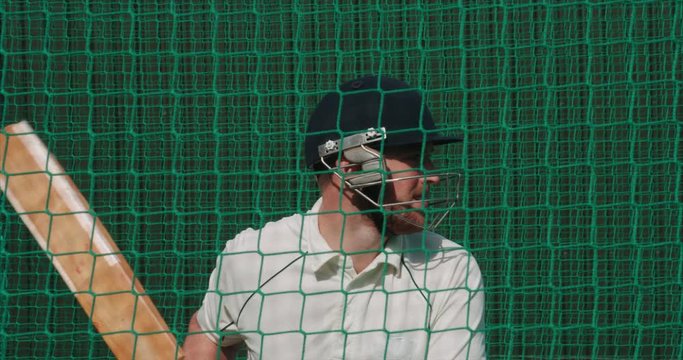 Cricketer hits cricket ball in nets.