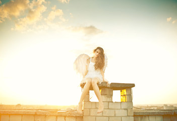 Warm evening sunlight illuminates pretty angel sitting on the ro