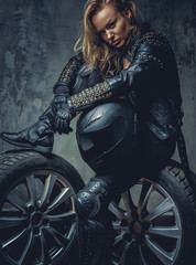 Fototapeta na wymiar Blonde female in leather clothes sits on a car's wheel .