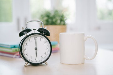 Vintage alarm clock with cup of coffee on wooden background,flare light,vintage tone