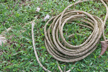 Coiled roll of rope arranged on grass ground with sunlight