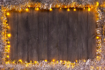 Christmas lights on a wooden background with free space. Frame with silver christmas chain.