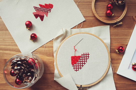 Christmas cross stitch designs and decorations on wooden table. Preparing handmade gifts for New Year and Christmas at home