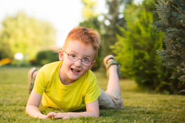 Naklejka na ściany i meble Happy baby boy with red hair in glasses on grass