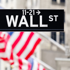 Wall street sign in New York City with american flags on the bac