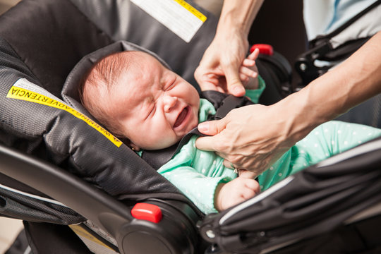 Crying baby being strapped to a stroller