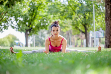 Naklejka na ściany i meble Young woman practicing yoga in the park on the green grass with