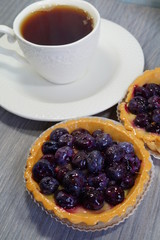 Tasty tart with blueberry and hot black tea in a white cup

