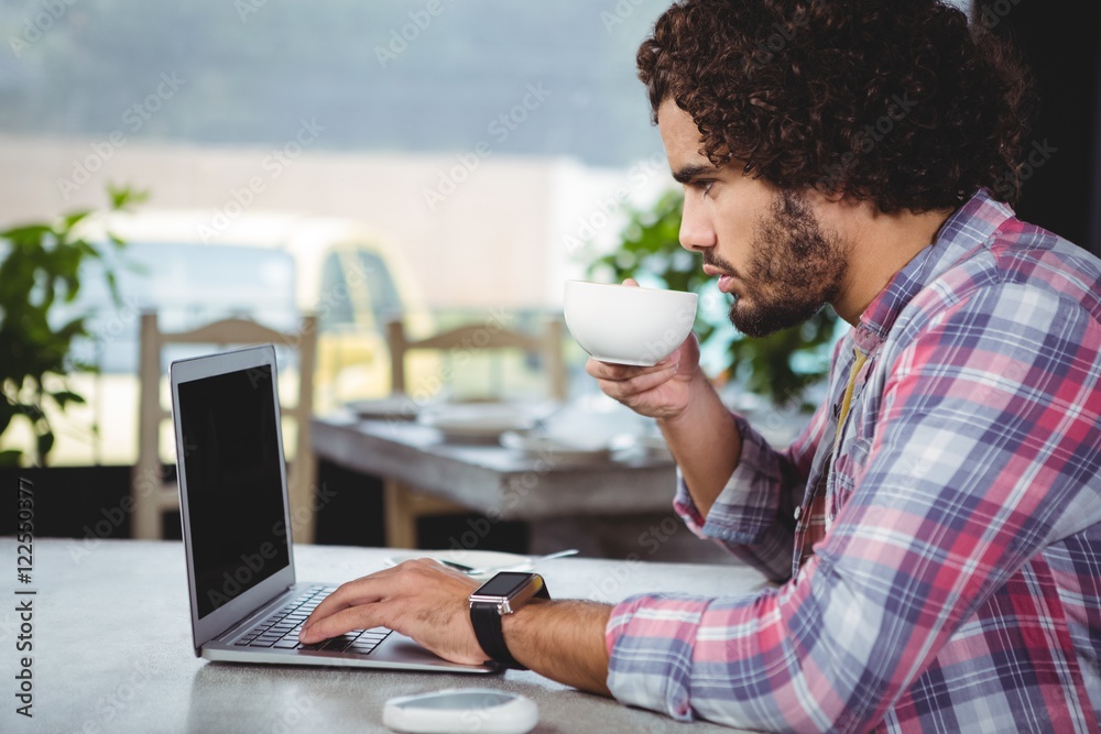 Poster man using laptop while having coffee