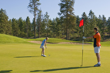 A junior female golfer gets ready to putt while her father readies the flagstick on a green at Two Eagles Golf Course in Westbank, British Columbia, Canada