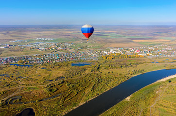Kaskara, Russia - October 1, 2016: Hot air balloon flying over river landscape at autumn day. Kaskara at background. Tyumen region