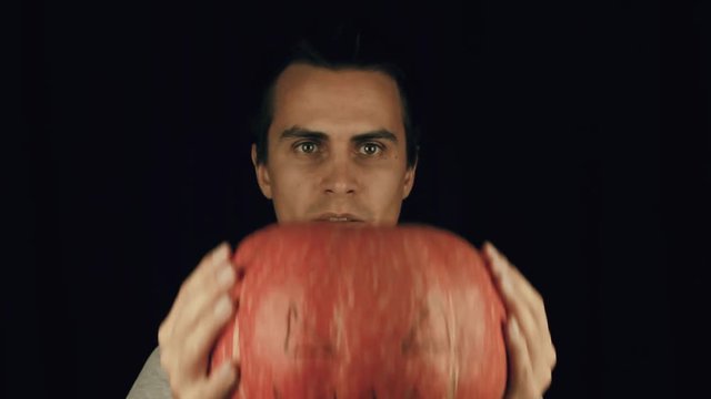 Guy in white t-shirt holding pumpking with drawn face, then put it down and make a creepy smile