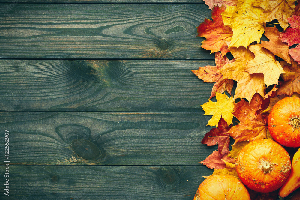 Wall mural Autumn leaves and pumpkins over old wooden background