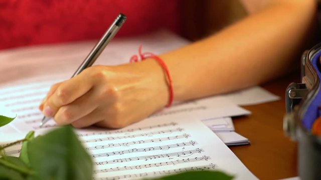 Girl composes music in music book . Girl write notes in pen your own sheet music . Camera moves from right to left.