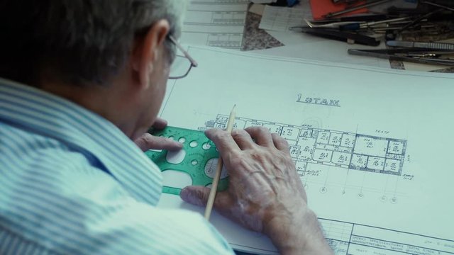 Architect at work. Drawing. Draftsman. Male architect. Architect puts a protractor to draw the line and drawing in pencil. Painstaking work. Design. Sketch. Protractor. Tools for drawing
