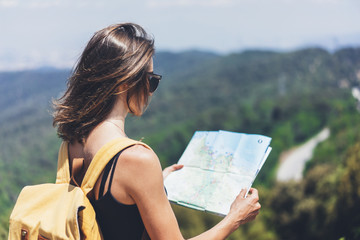 Hipster young girl with bright backpack enjoying panoramic mountain sea, using map and looking...