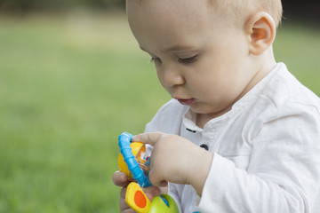 Little pretty boy plays with a toy on green grass  in summer park outdoors.